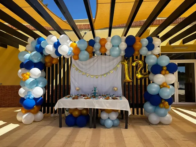 Mesa de doces e arco de balões azuis e dourados ao ar livre, evento organizado pela Criar Eventos.