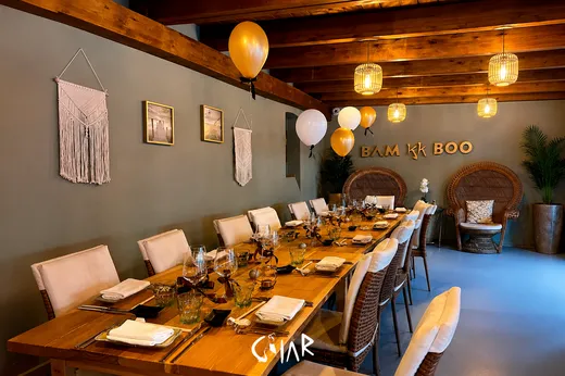 Mesa comprida decorada para um jantar de grupo, com balões dourados e detalhes artesanais.