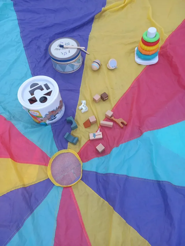 Crianças a brincar com um paraquedas de cores e brinquedos de madeira, numa animação da Criar Eventos.